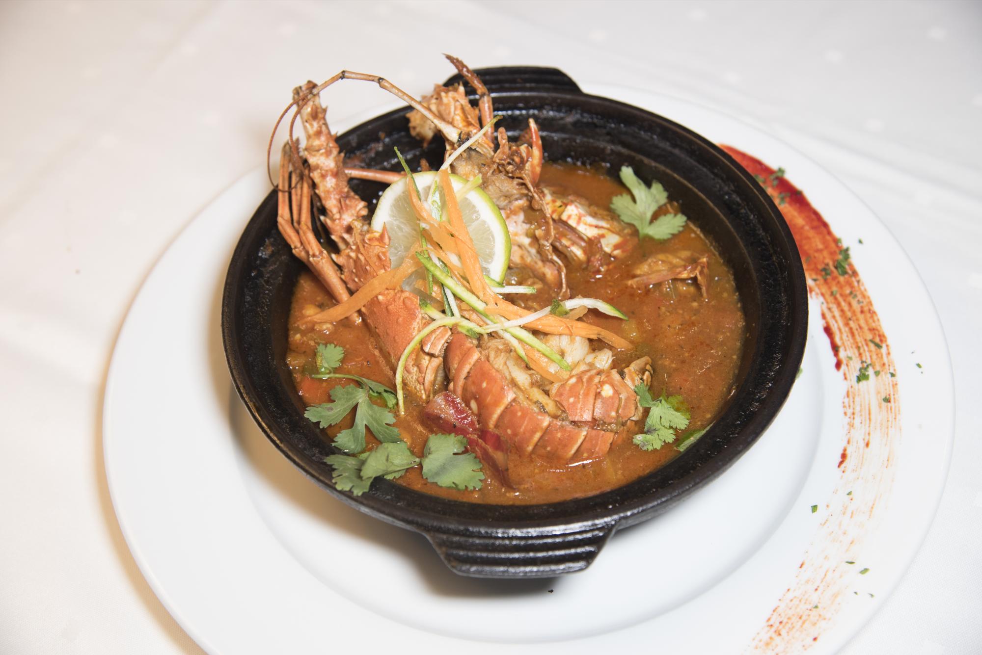 Caldera de langosta. Con salsa a base de tomates frescos, ajo, caldo de pescado y cebolla; y provisto de tostones.