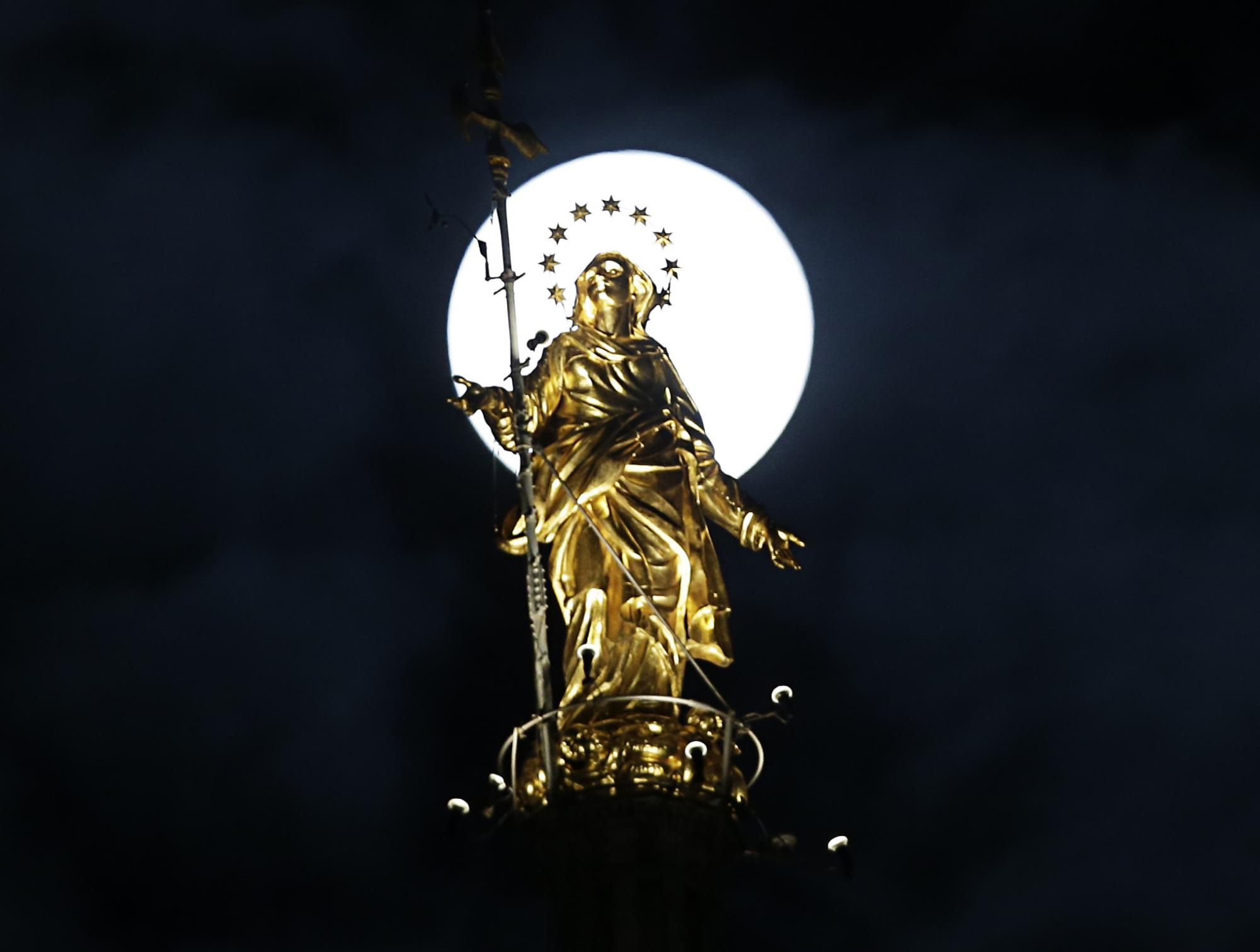 La superluna detrás de la estatua de Santa María en Milán Italia