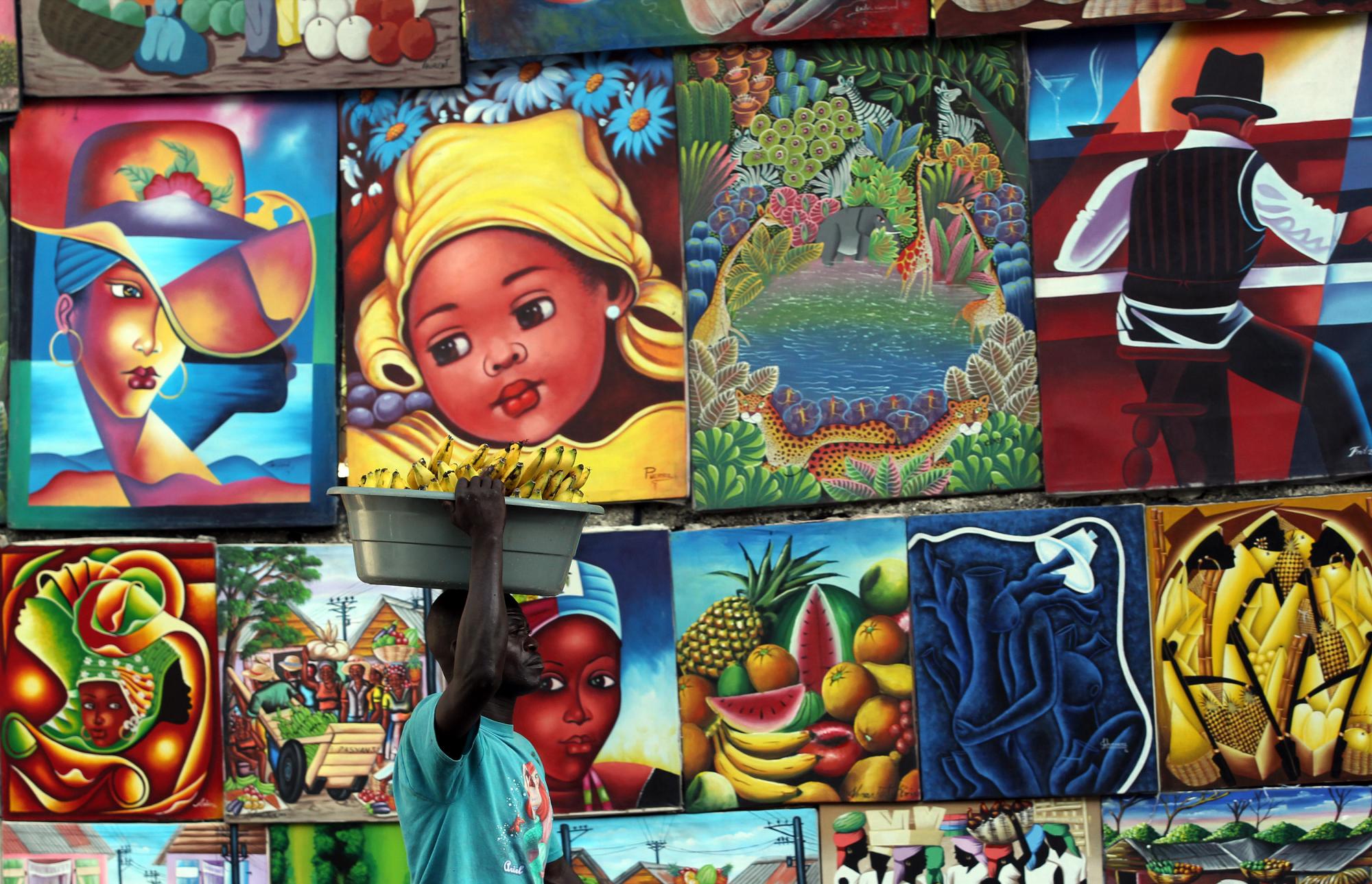 Un vendedor de bananas pasa junto a un puesto callejero de venta de pinturas en Puerto Príncipe.