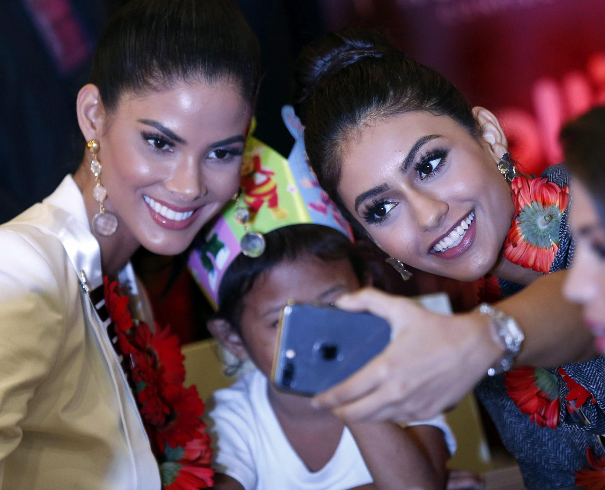 La candidata dominicana Sal García (i) y la candidata malasia Kiran Jassal (d) posan para un selfi junto a un niño huérfano durante un evento en Pasay, al sur de Manila en Filipinas.