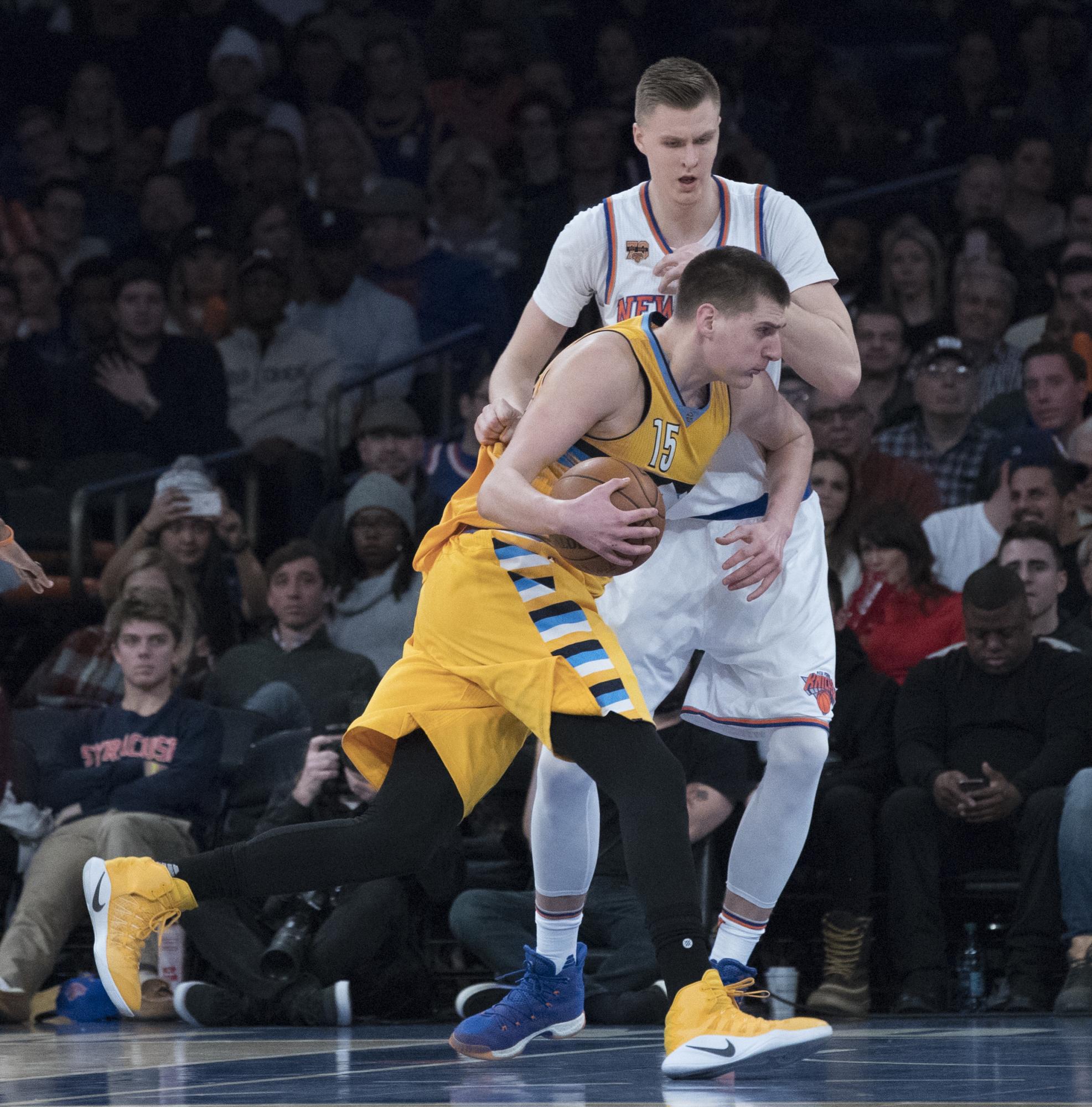 Nikola Jokic (primer plano) conduce el balón hacia la canasta contra el delantero Kristaps Porzingis.
