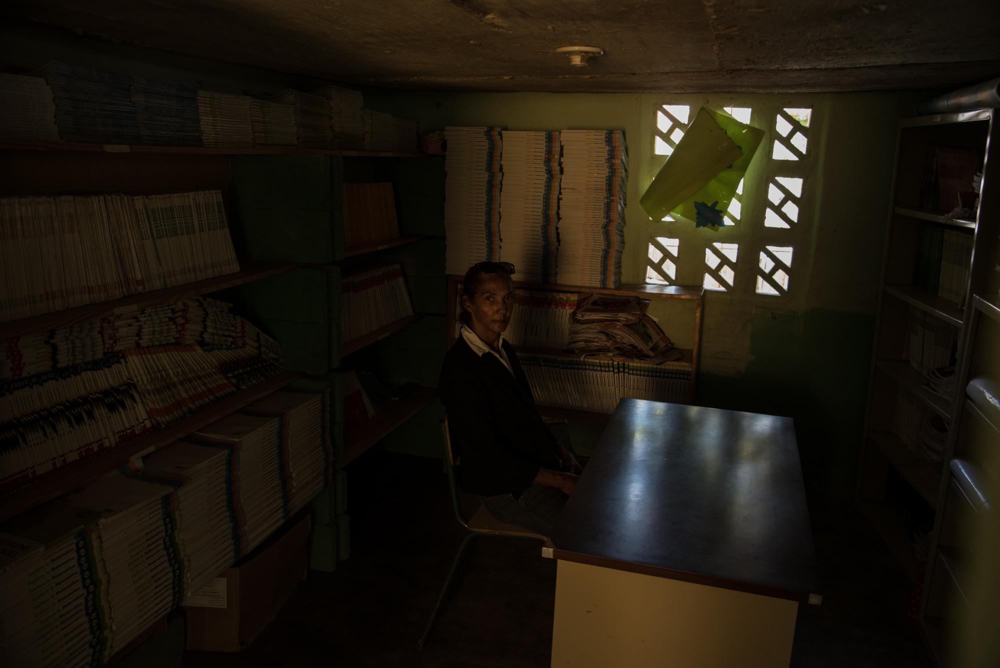 Una maestra sentada en la biblioteca de la Escuela Inicial y Básica Doctor Clarence Cristopher Hamilton Oxley, que funciona en una casa alquilada.