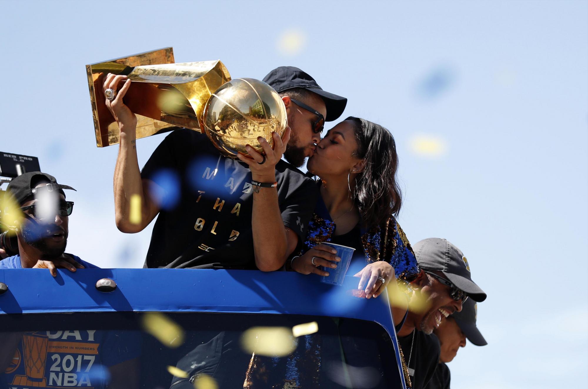 El jugador de Golden State Warriors Stephen Curry (i) besa a su esposa Ayesha (d) mientras levanta el trofeo del Campeonato Larry OBrien.