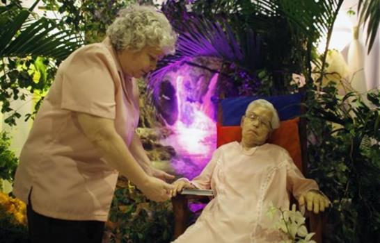 La velan sentada en su mecedora y con su vestido de bodas