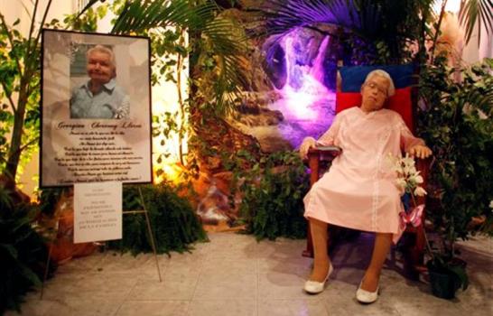 La velan sentada en su mecedora y con su vestido de bodas